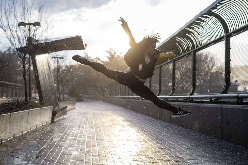 《自媒體斜槓一年,我多存了250萬!》讀後心得 4 A dancer leaps gracefully on a rainy day, backlit by the setting sun in an urban environment.
