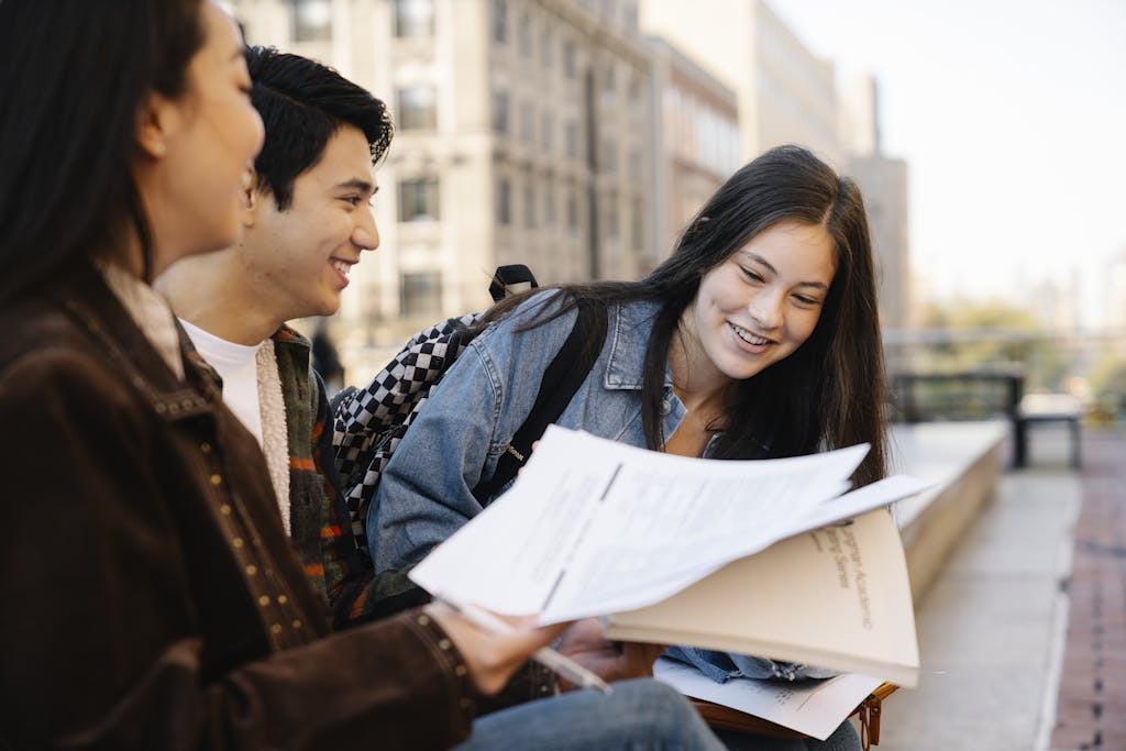 《成為更好的自己》讀後心得:劉軒給青少年的心理必修課 2 Teen students engage in outdoor study session, sharing documents and smiling.