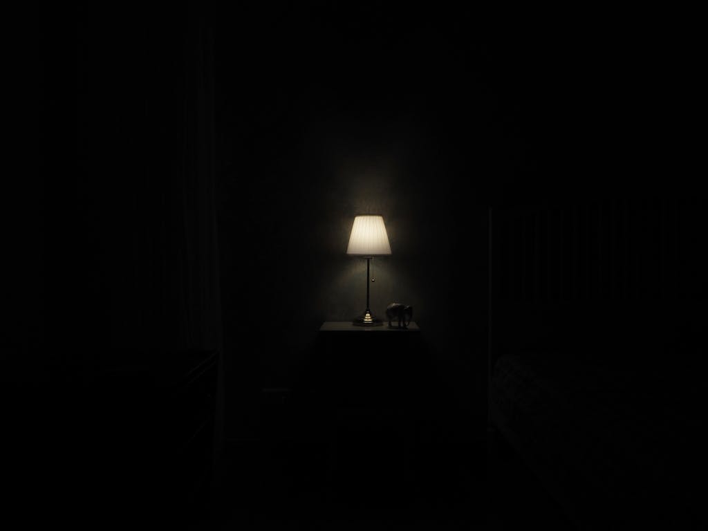 《有時幸,有時傷》讀後心得:書寫不是為了讓生活變完美 3 Illuminated lamp on nightstand casting a warm glow in a dark, minimalist room.
