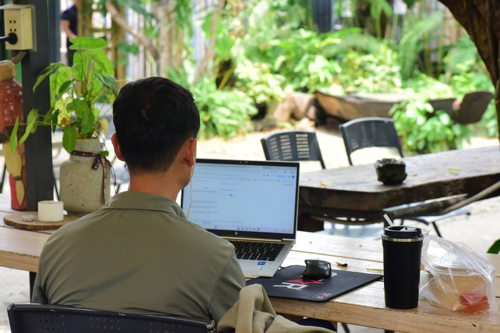 A young man using a laptop in an outdoor garden setting, focused on work.